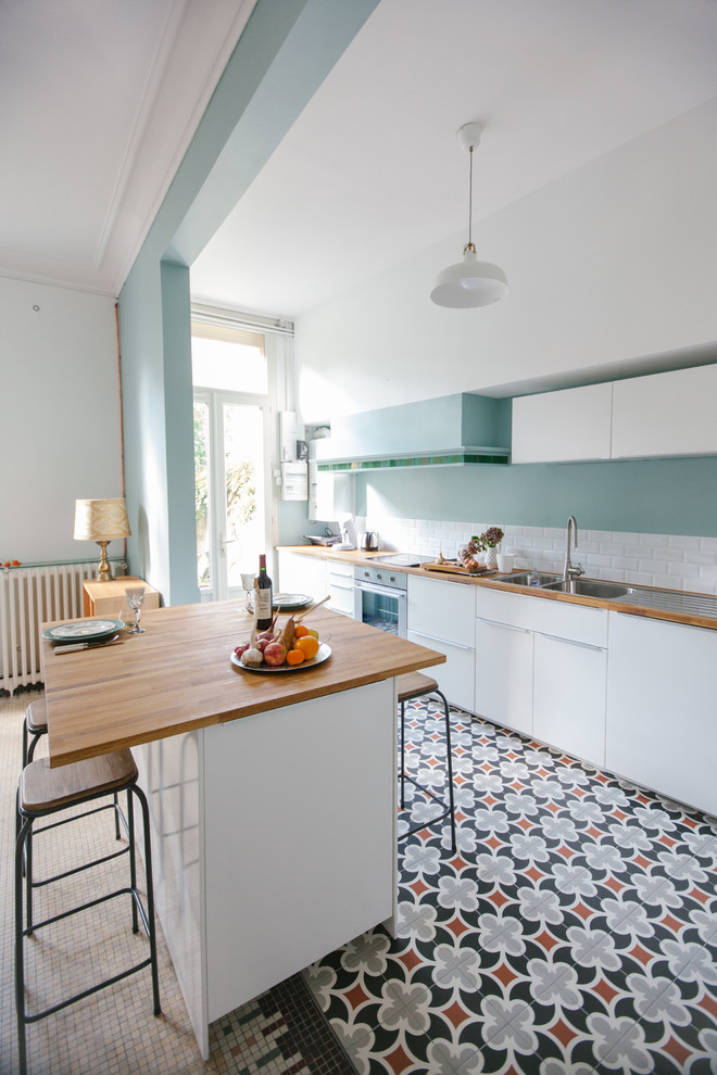 This is an example of a large contemporary single-wall eat-in kitchen in Bordeaux with a double-bowl sink, flat-panel cabinets, white cabinets, wood benchtops, white splashback, subway tile splashback, stainless steel appliances, ceramic floors and with island.