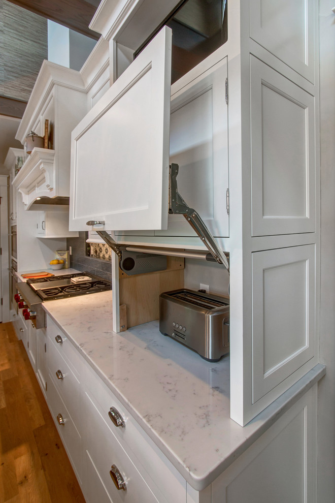 This is an example of an expansive transitional u-shaped eat-in kitchen in Milwaukee with a farmhouse sink, recessed-panel cabinets, white cabinets, quartz benchtops, grey splashback, ceramic splashback, panelled appliances, light hardwood floors and with island.