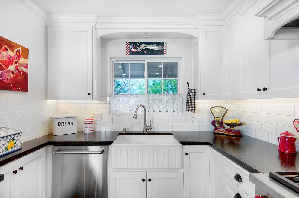 Mid-sized country u-shaped open plan kitchen in San Francisco with a farmhouse sink, shaker cabinets, white cabinets, white splashback, subway tile splashback, stainless steel appliances, medium hardwood floors, a peninsula, brown floor and black benchtop.