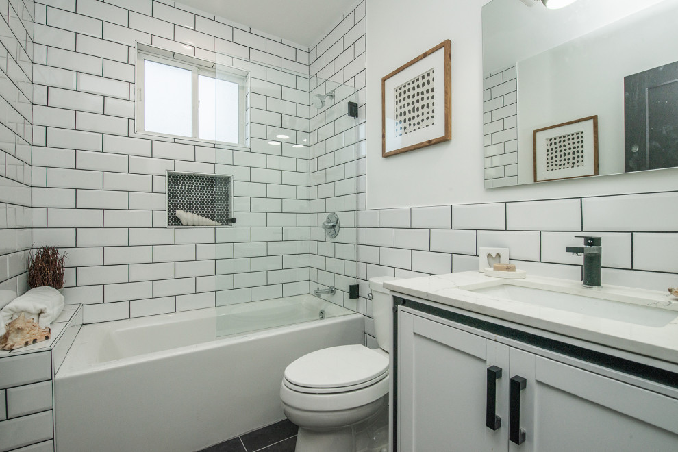 Aménagement d'une petite salle d'eau moderne avec un placard à porte shaker, des portes de placard blanches, une baignoire en alcôve, un combiné douche/baignoire, WC séparés, un carrelage blanc, un carrelage métro, un mur blanc, un sol en carrelage de porcelaine, un lavabo encastré, un plan de toilette en quartz modifié, un sol noir, une cabine de douche à porte battante, un plan de toilette blanc, une niche, meuble simple vasque, meuble-lavabo sur pied et boiseries.