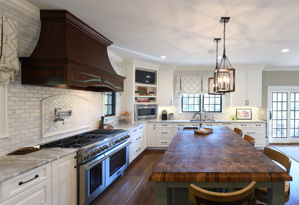 Example of a large transitional l-shaped dark wood floor and brown floor kitchen design with an undermount sink, raised-panel cabinets, white cabinets, quartzite countertops, white backsplash, marble backsplash, stainless steel appliances and an island