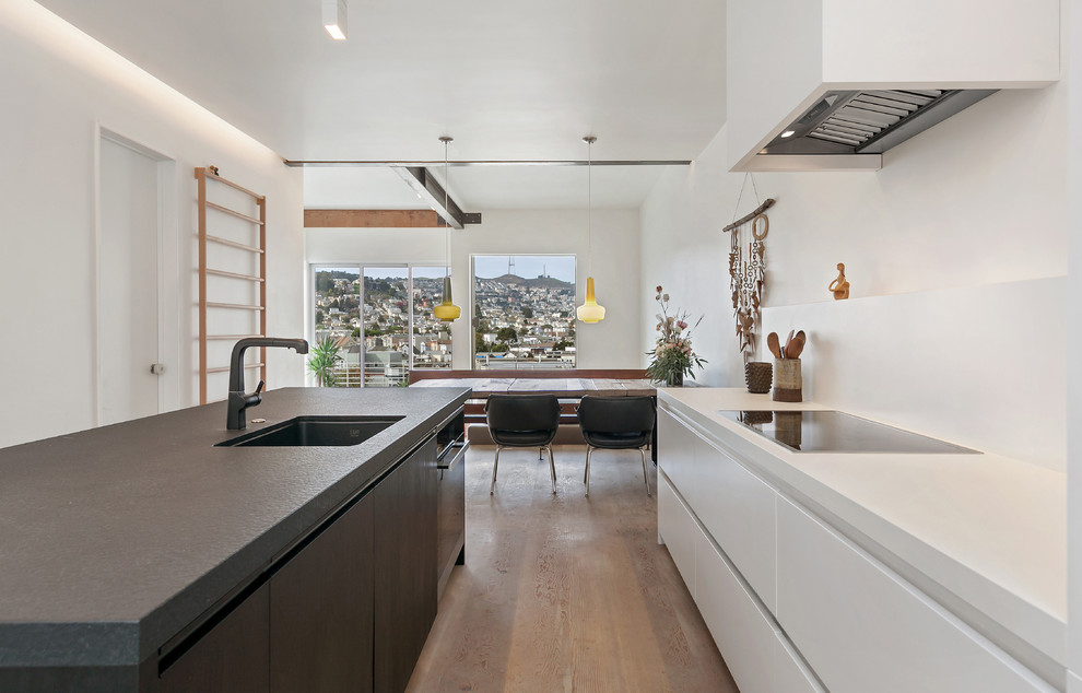 Photo of a large scandinavian galley kitchen pantry in San Francisco with an integrated sink, flat-panel cabinets, white cabinets, granite benchtops, white appliances, light hardwood floors and with island.