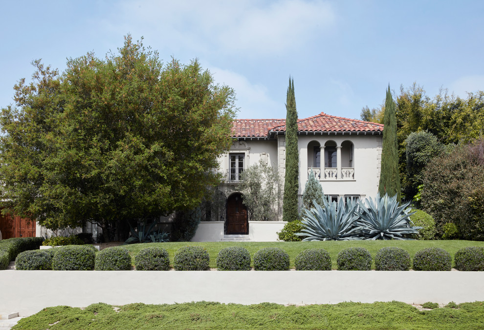 This is an example of a large mediterranean two-storey stucco white house exterior in Los Angeles with a hip roof, a tile roof and a red roof.