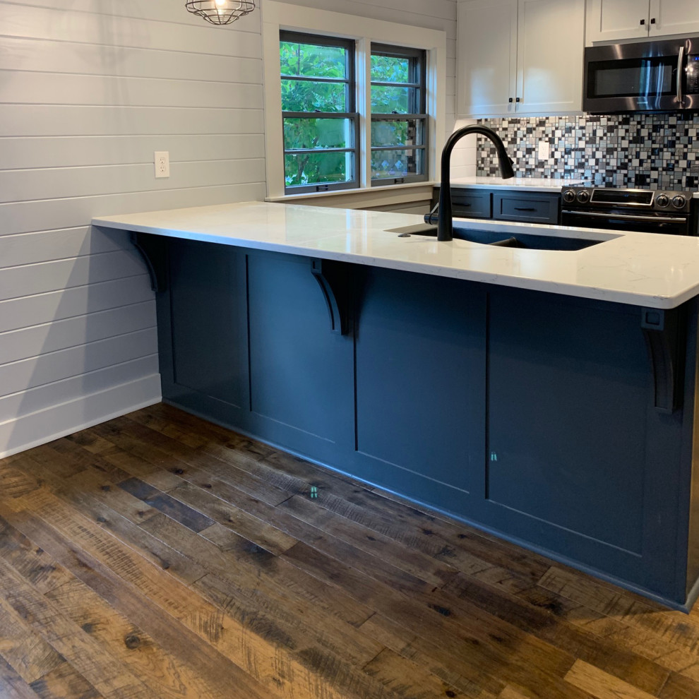 This is an example of a country eat-in kitchen in Los Angeles with a farmhouse sink, shaker cabinets, blue cabinets, granite benchtops, grey splashback, glass tile splashback, stainless steel appliances, medium hardwood floors, with island, brown floor, white benchtop and timber.