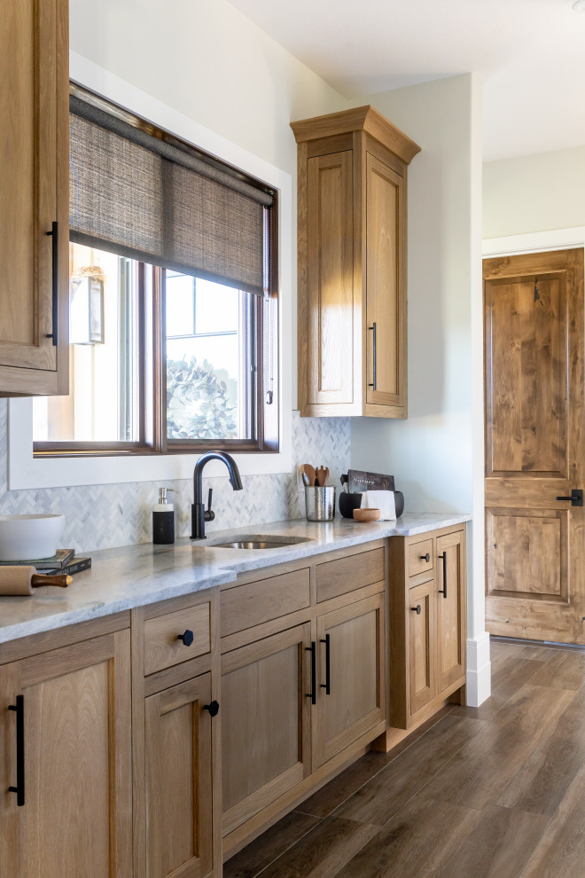 Inspiration for a country eat-in kitchen in Salt Lake City with a farmhouse sink, beaded inset cabinets, medium wood cabinets, white splashback, black appliances, dark hardwood floors, brown floor, black benchtop, marble benchtops, stone tile splashback and multiple islands.