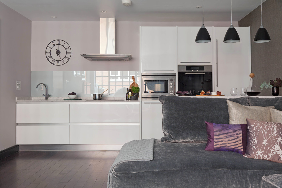 Photo of a small contemporary galley kitchen/diner in London with a single-bowl sink, flat-panel cabinets, white cabinets, engineered stone countertops, grey splashback, glass sheet splashback, stainless steel appliances, dark hardwood flooring and a breakfast bar.