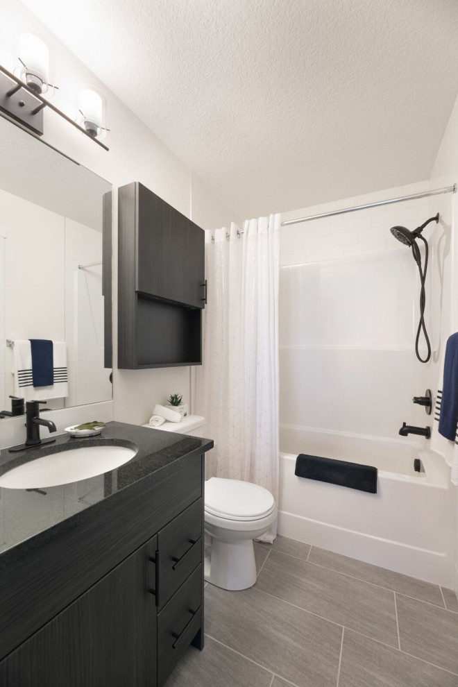 Modern bathroom in Calgary with flat-panel cabinets, black cabinets, an alcove tub, a shower/bathtub combo, a two-piece toilet, white tile, white walls, an undermount sink, grey floor, a shower curtain and black benchtops.