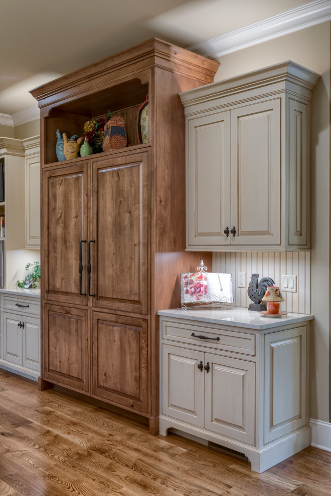 Inspiration for an expansive country l-shaped kitchen in Other with a farmhouse sink, raised-panel cabinets, beige cabinets, granite benchtops, beige splashback, ceramic splashback, panelled appliances, medium hardwood floors, with island, brown floor and beige benchtop.