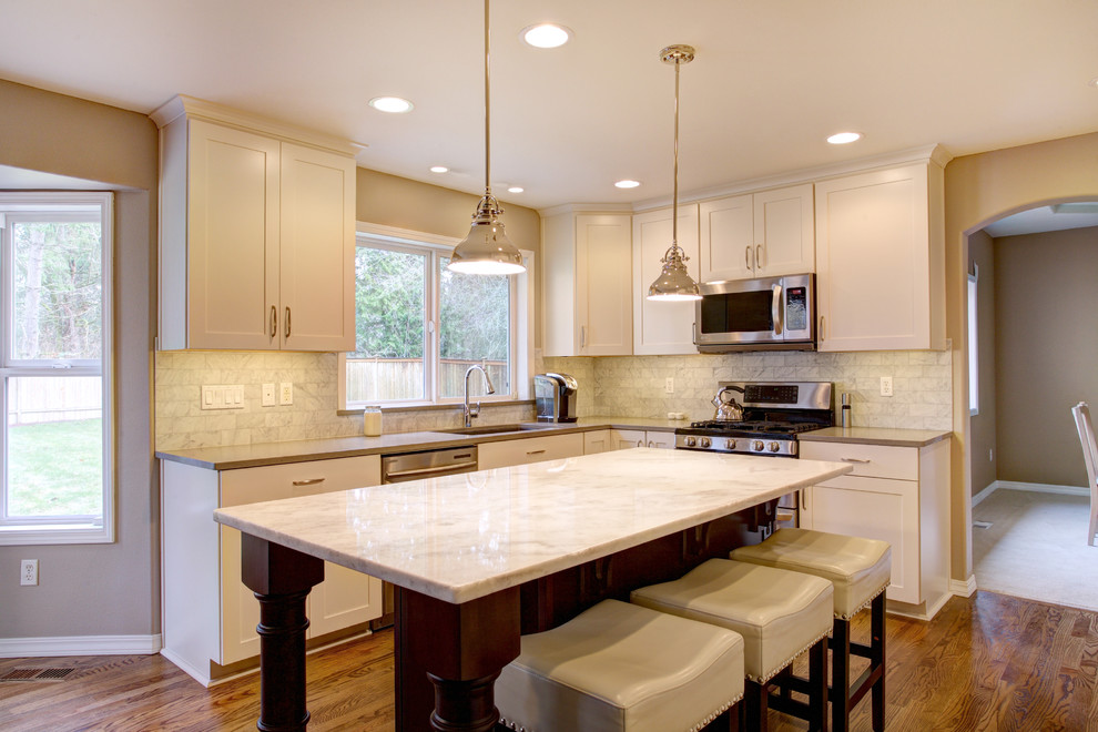 Inspiration for a mid-sized transitional l-shaped medium tone wood floor eat-in kitchen remodel in Seattle with an undermount sink, recessed-panel cabinets, white cabinets, quartz countertops, white backsplash, stone tile backsplash, stainless steel appliances and an island