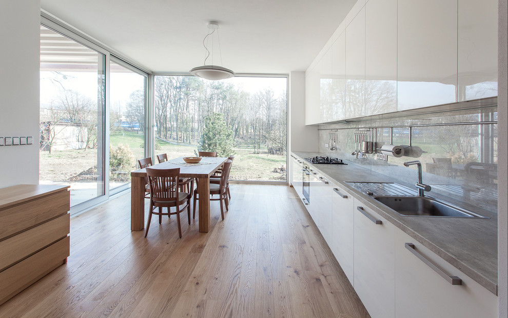 Large modern single-wall eat-in kitchen in Other with a drop-in sink, flat-panel cabinets, white cabinets, laminate benchtops, grey splashback, black appliances, light hardwood floors and no island.