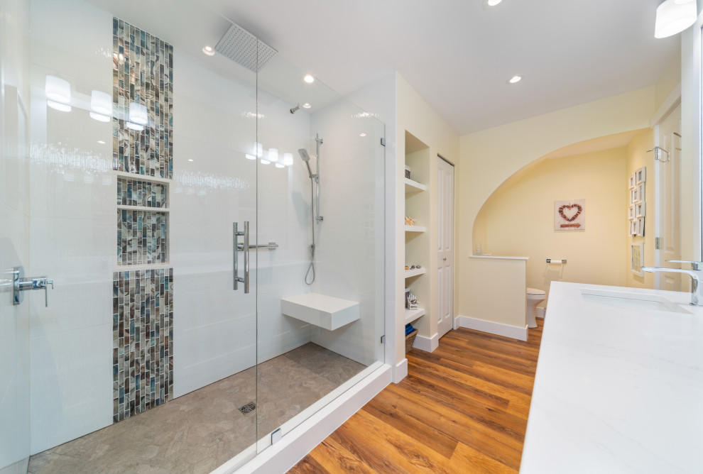 Inspiration for a mid-sized beach style master bathroom in Vancouver with shaker cabinets, white cabinets, white tile, white walls, medium hardwood floors, an undermount sink, engineered quartz benchtops, brown floor, a hinged shower door, white benchtops, a niche, a double vanity and a built-in vanity.