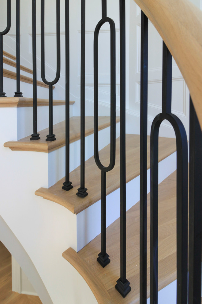 This is an example of an expansive transitional wood curved staircase in DC Metro with wood risers, mixed railing and decorative wall panelling.