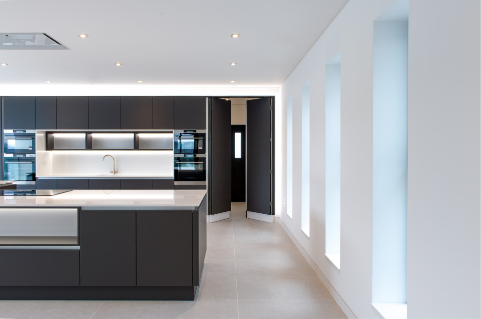 Inspiration for a large contemporary single-wall open plan kitchen in Cornwall with a built-in sink, flat-panel cabinets, grey cabinets, composite countertops, white splashback, black appliances, cement flooring, an island, beige floors and white worktops.