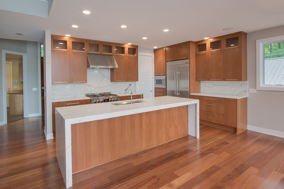 Transitional l-shaped medium tone wood floor kitchen photo in Grand Rapids with a double-bowl sink, flat-panel cabinets, medium tone wood cabinets, granite countertops, white backsplash, stone slab backsplash, stainless steel appliances and an island