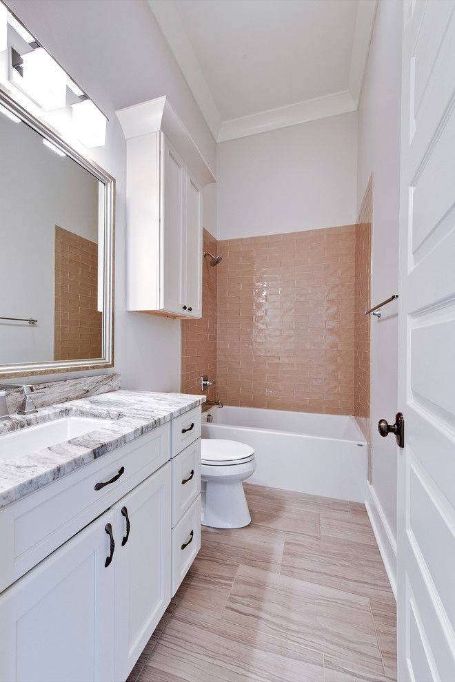 Inspiration for a mid-sized country 3/4 bathroom in New Orleans with shaker cabinets, white cabinets, an alcove tub, a shower/bathtub combo, a one-piece toilet, brown tile, subway tile, grey walls, dark hardwood floors, a pedestal sink, granite benchtops and brown floor.