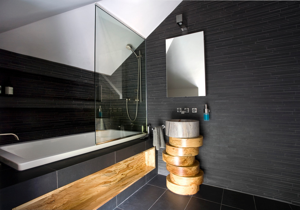 Design ideas for a contemporary bathroom in London with a drop-in tub, black tile, black walls and a vessel sink.
