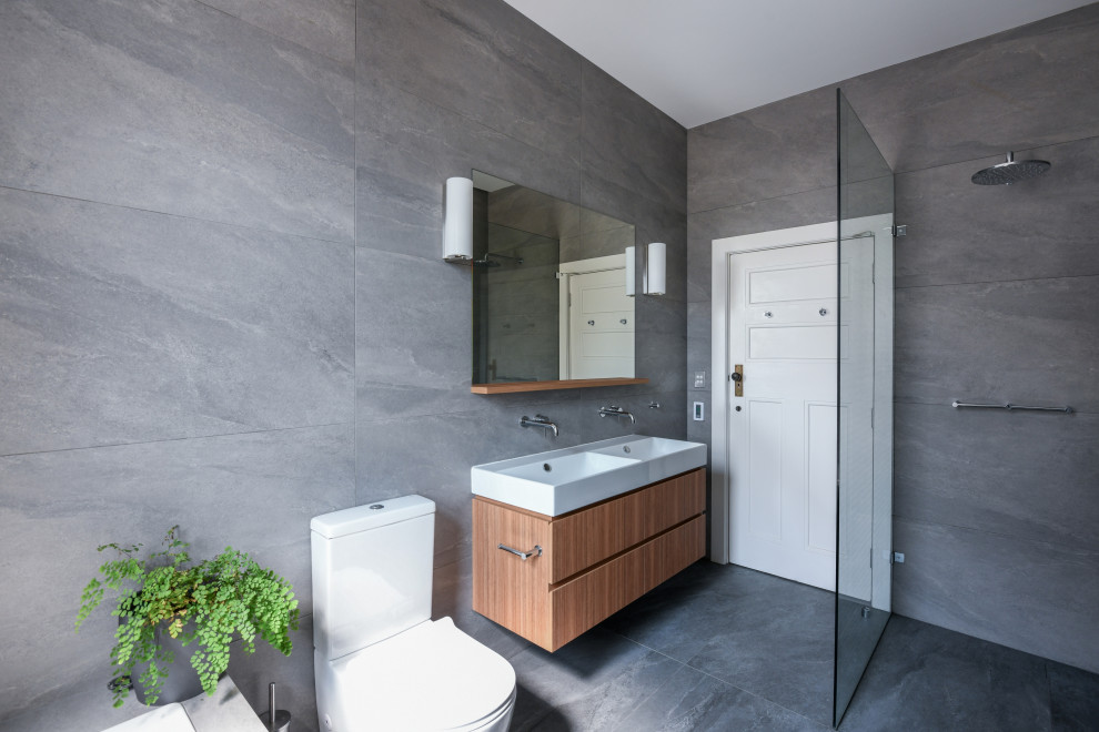 This is an example of a large modern master bathroom in Sydney with flat-panel cabinets, medium wood cabinets, an open shower, a one-piece toilet, gray tile, ceramic tile, grey walls, ceramic floors, a wall-mount sink, grey floor, an open shower and white benchtops.