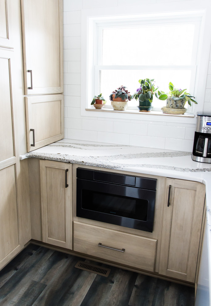 Mid-sized transitional u-shaped vinyl floor and brown floor enclosed kitchen photo with an undermount sink, flat-panel cabinets, beige cabinets, quartz countertops, white backsplash, subway tile backsplash, black appliances, a peninsula and white countertops