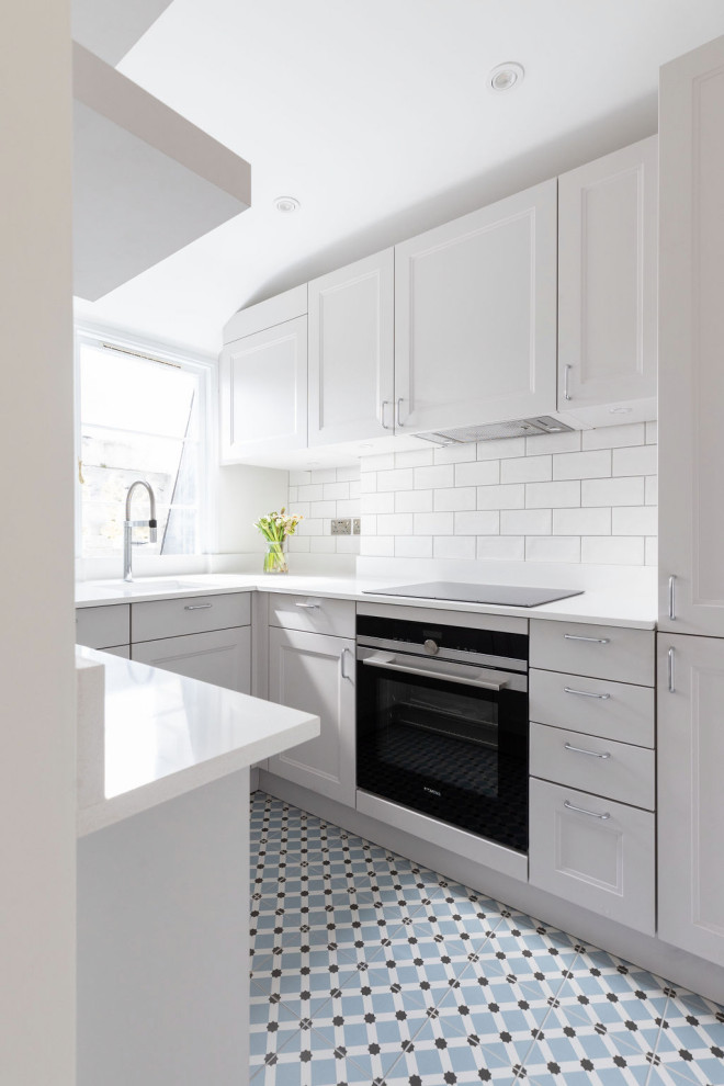 Cette image montre une petite cuisine ouverte grise et blanche minimaliste avec des portes de placard grises, une crédence blanche, une crédence en céramique, un électroménager en acier inoxydable, aucun îlot, un sol multicolore et un plan de travail blanc.