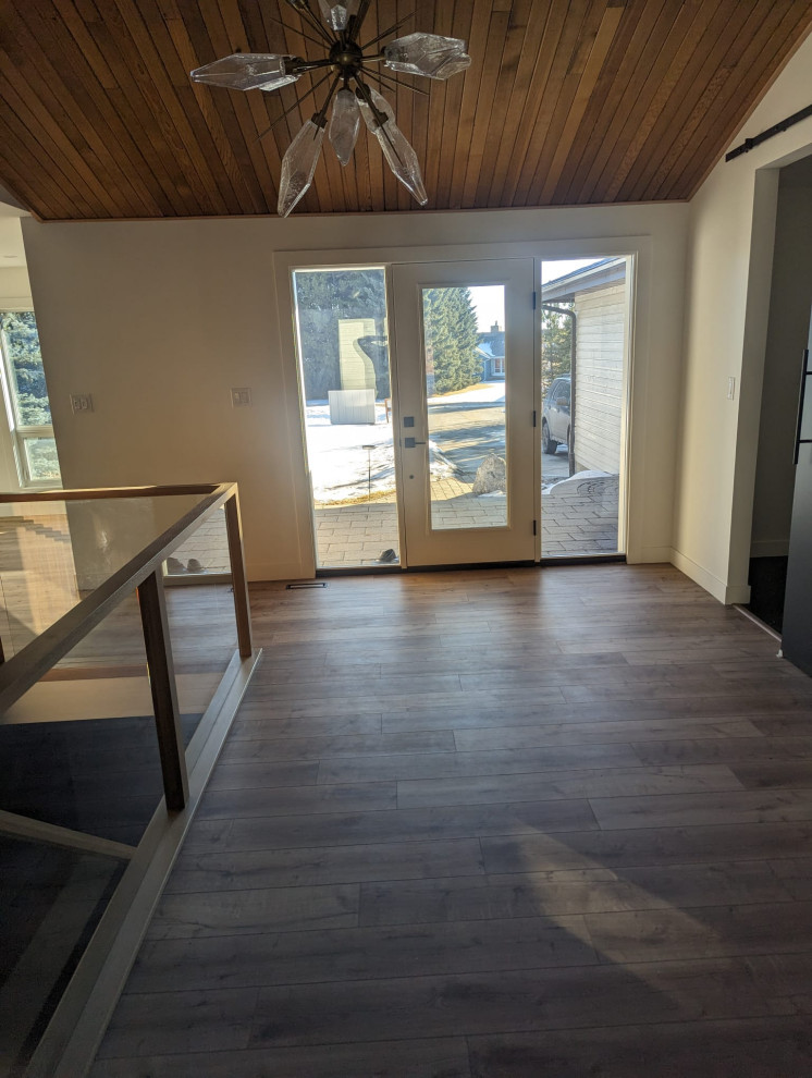 Design ideas for a large midcentury entryway in Edmonton with white walls, vinyl floors, a single front door, a white front door, brown floor and wood.