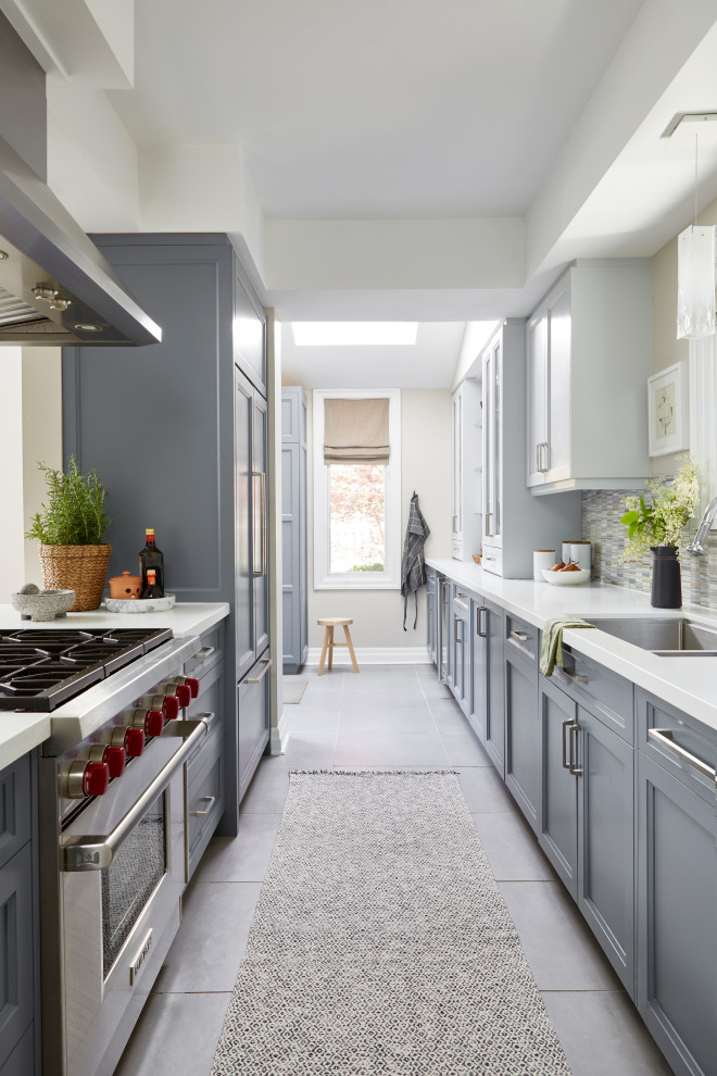 Inspiration for a medium sized traditional galley kitchen/diner in Toronto with a submerged sink, shaker cabinets, grey cabinets, engineered stone countertops, multi-coloured splashback, marble splashback, integrated appliances, porcelain flooring, a breakfast bar, grey floors and white worktops.