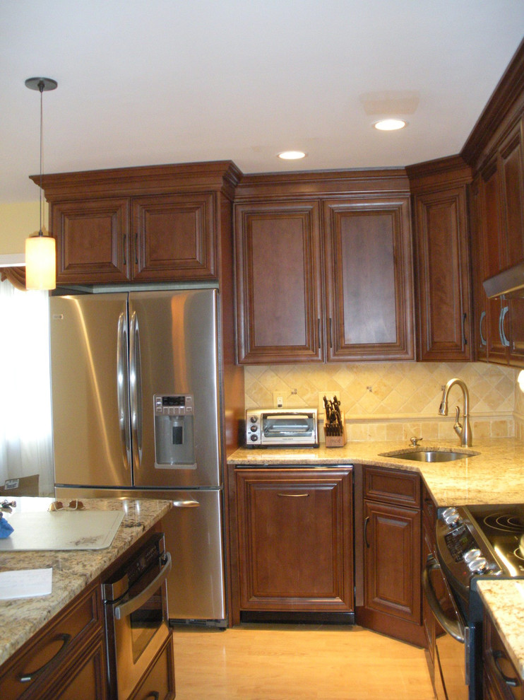 This is an example of a mid-sized traditional l-shaped eat-in kitchen in Philadelphia with an undermount sink, raised-panel cabinets, medium wood cabinets, granite benchtops, beige splashback, stone tile splashback, stainless steel appliances, light hardwood floors and with island.