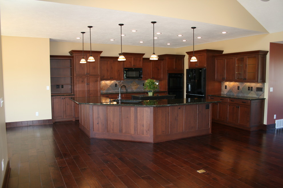 Photo of a mid-sized arts and crafts l-shaped open plan kitchen in Omaha with an undermount sink, shaker cabinets, dark wood cabinets, granite benchtops, black appliances, dark hardwood floors, with island, beige splashback, ceramic splashback and brown floor.
