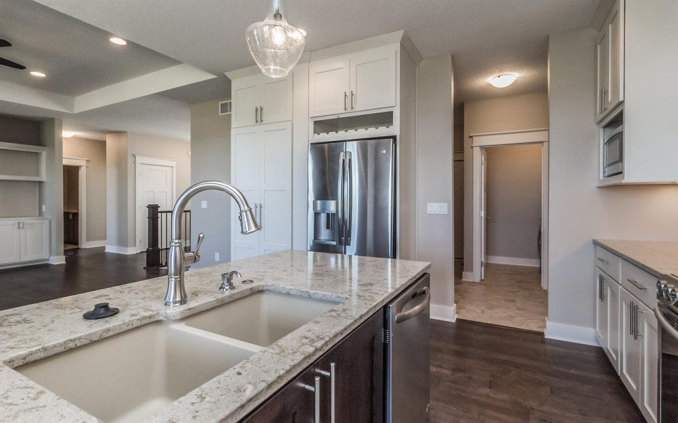 Example of a transitional l-shaped medium tone wood floor and brown floor eat-in kitchen design with an undermount sink, shaker cabinets, white cabinets, quartz countertops, ceramic backsplash, stainless steel appliances and an island
