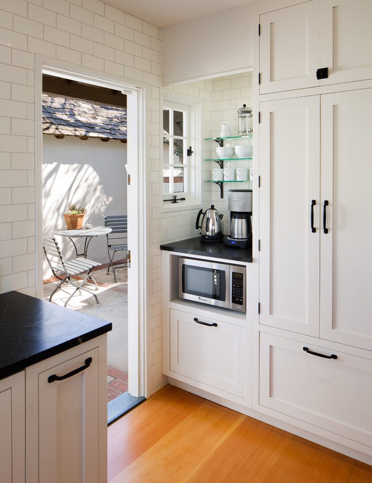 Inspiration for a mid-sized traditional l-shaped eat-in kitchen in San Diego with a single-bowl sink, shaker cabinets, white cabinets, soapstone benchtops, white splashback, subway tile splashback, panelled appliances, medium hardwood floors and with island.