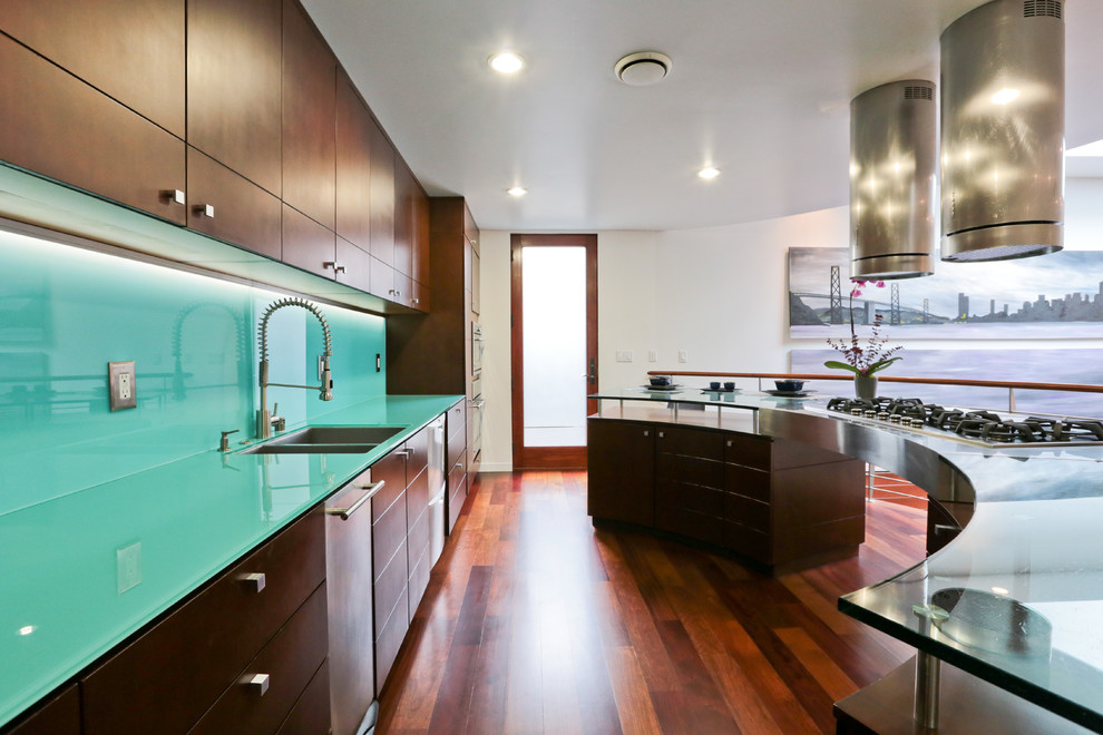 Photo of a mid-sized modern u-shaped open plan kitchen in San Francisco with an undermount sink, flat-panel cabinets, dark wood cabinets, glass benchtops, blue splashback, glass tile splashback, stainless steel appliances, medium hardwood floors, with island and brown floor.