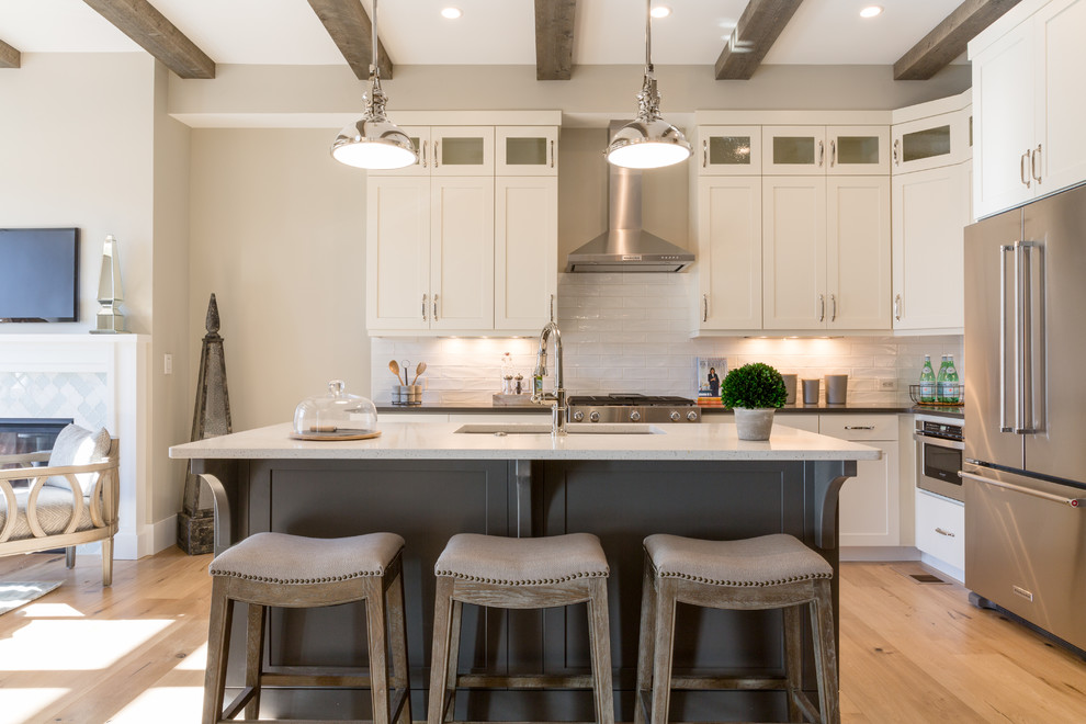 Design ideas for an industrial eat-in kitchen in Denver with an undermount sink, shaker cabinets, white cabinets, quartzite benchtops, white splashback, ceramic splashback, stainless steel appliances, light hardwood floors and with island.