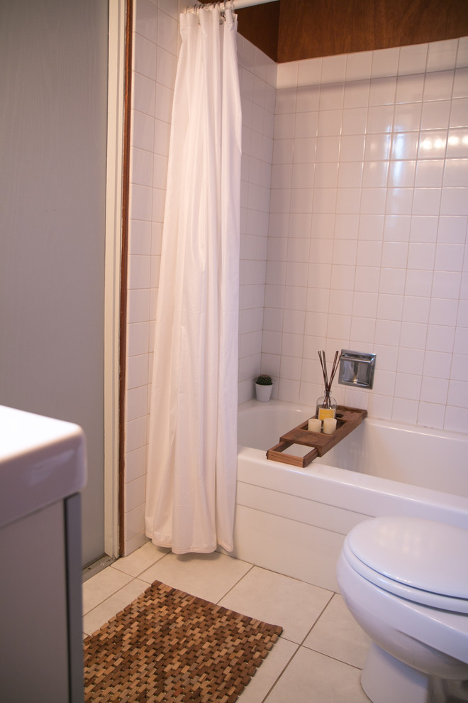 This is an example of a midcentury bathroom in San Francisco with glass-front cabinets, grey cabinets, a drop-in tub, a shower/bathtub combo, a one-piece toilet, white tile, ceramic tile, brown walls, ceramic floors, a console sink, white floor and a shower curtain.