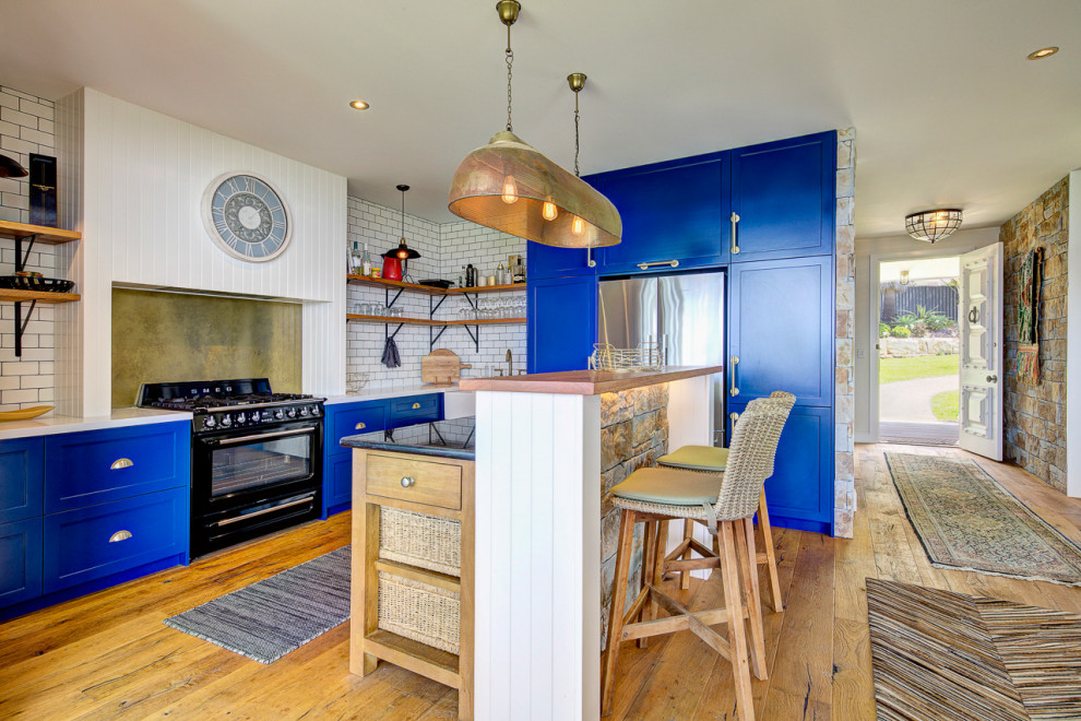 Maritime Küche in L-Form mit Schrankfronten im Shaker-Stil, blauen Schränken, Küchenrückwand in Weiß, Rückwand aus Metrofliesen, braunem Holzboden, Kücheninsel und weißer Arbeitsplatte in Sydney