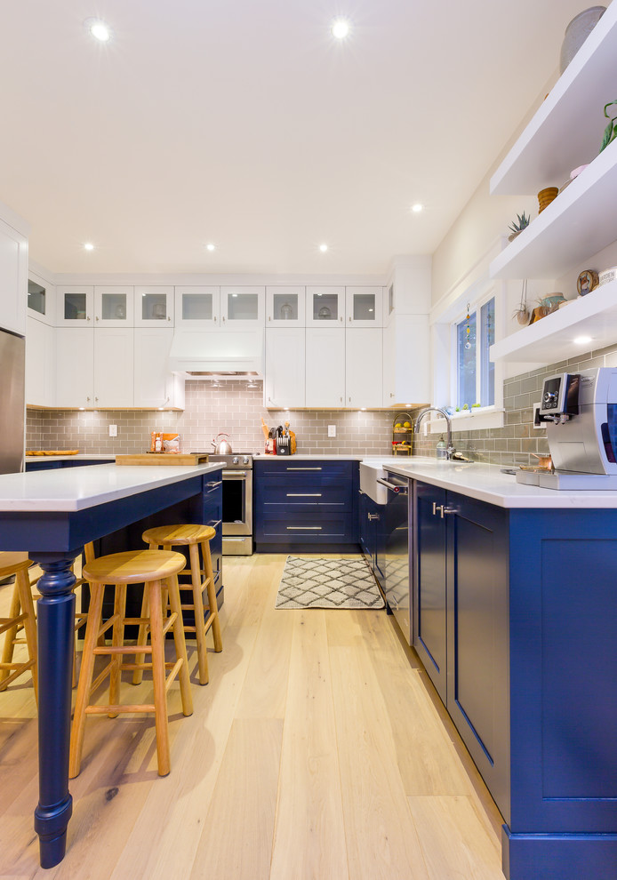 Inspiration for a large transitional u-shaped light wood floor open concept kitchen remodel with a farmhouse sink, shaker cabinets, blue cabinets, quartz countertops, gray backsplash, glass tile backsplash, stainless steel appliances, an island and white countertops