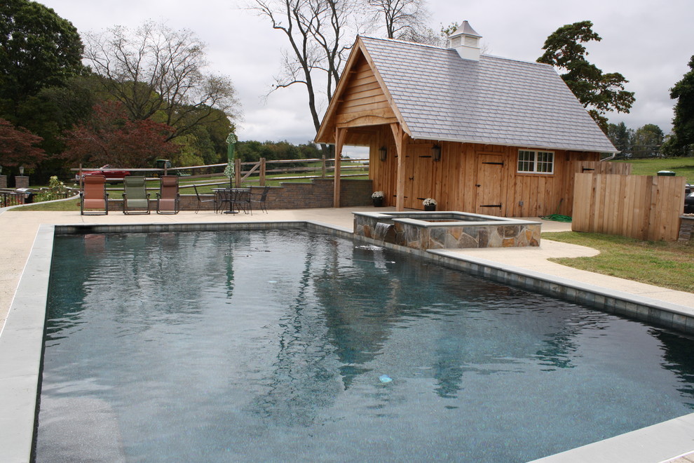 Large country side yard pool in Philadelphia with a water feature and concrete pavers.
