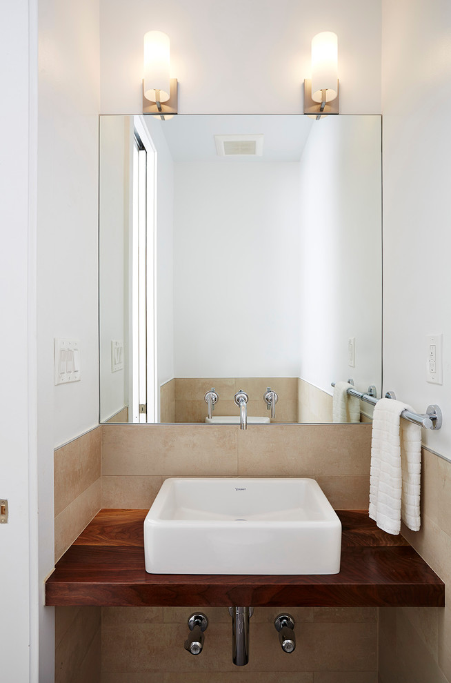Design ideas for a small contemporary powder room in New York with a two-piece toilet, beige tile, ceramic tile, white walls, a vessel sink, wood benchtops, porcelain floors, beige floor and brown benchtops.