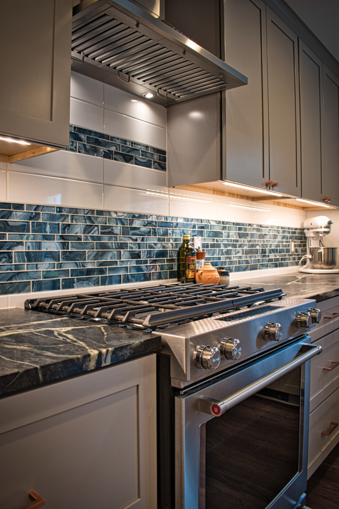 Photo of a mid-sized country l-shaped eat-in kitchen in Other with shaker cabinets, grey cabinets, soapstone benchtops, blue splashback, glass tile splashback, stainless steel appliances, vinyl floors, with island, brown floor and multi-coloured benchtop.