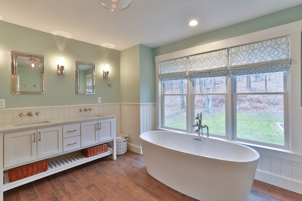Large transitional master bathroom in New York with shaker cabinets, white cabinets, a freestanding tub, blue walls, medium hardwood floors, an undermount sink, marble benchtops, brown floor, an alcove shower, a two-piece toilet and a hinged shower door.