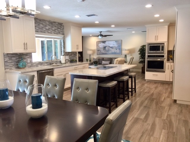 This is an example of a mid-sized transitional u-shaped open plan kitchen in Phoenix with an undermount sink, shaker cabinets, white cabinets, grey splashback, matchstick tile splashback, stainless steel appliances, vinyl floors, with island, granite benchtops and brown floor.