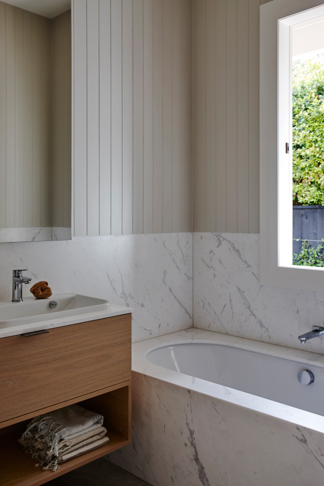 Inspiration for a small modern master bathroom in Auckland with an undermount tub, white tile, marble, grey walls, solid surface benchtops, white benchtops, a single vanity, a floating vanity, planked wall panelling, flat-panel cabinets, medium wood cabinets and a drop-in sink.