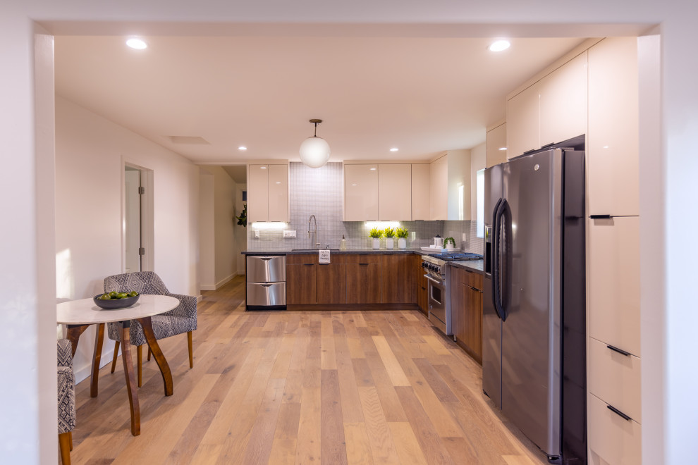 This is an example of a large contemporary l-shaped kitchen pantry in Los Angeles with a double-bowl sink, flat-panel cabinets, beige cabinets, quartz benchtops, blue splashback, cement tile splashback, stainless steel appliances, medium hardwood floors, brown floor and grey benchtop.