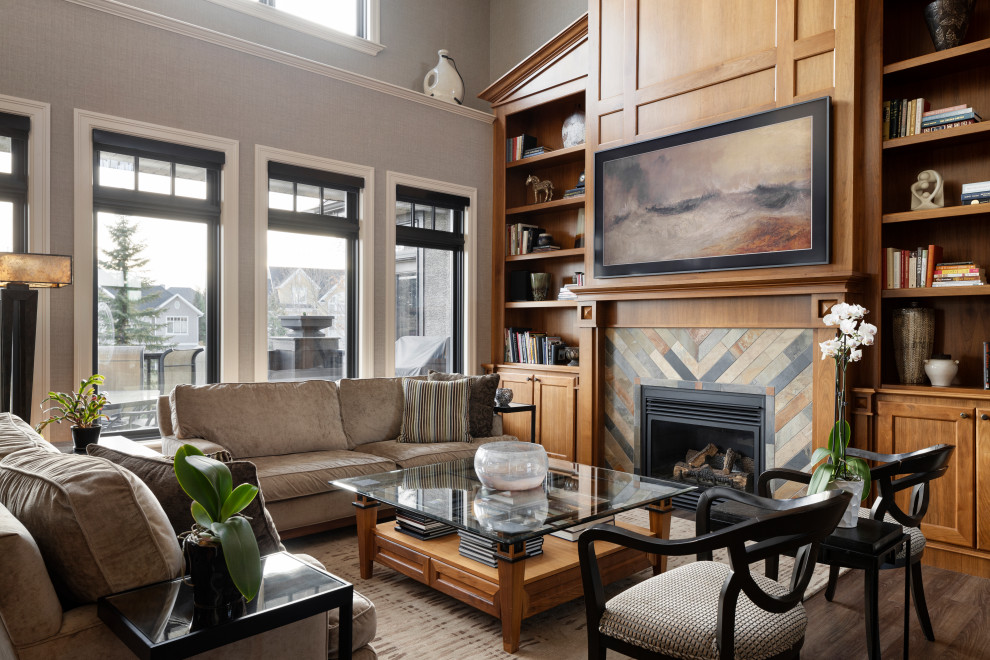 Großes, Offenes Klassisches Wohnzimmer mit grauer Wandfarbe, braunem Holzboden, Kamin, Kaminumrandung aus Stein, TV-Wand, braunem Boden, gewölbter Decke und Tapetenwänden in Calgary