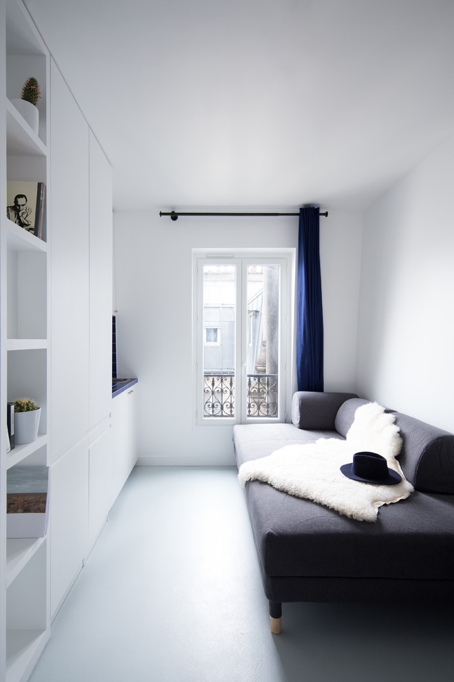 Photo of a small scandinavian open concept living room in Paris with a library, white walls, concrete floors, no fireplace, a freestanding tv and grey floor.