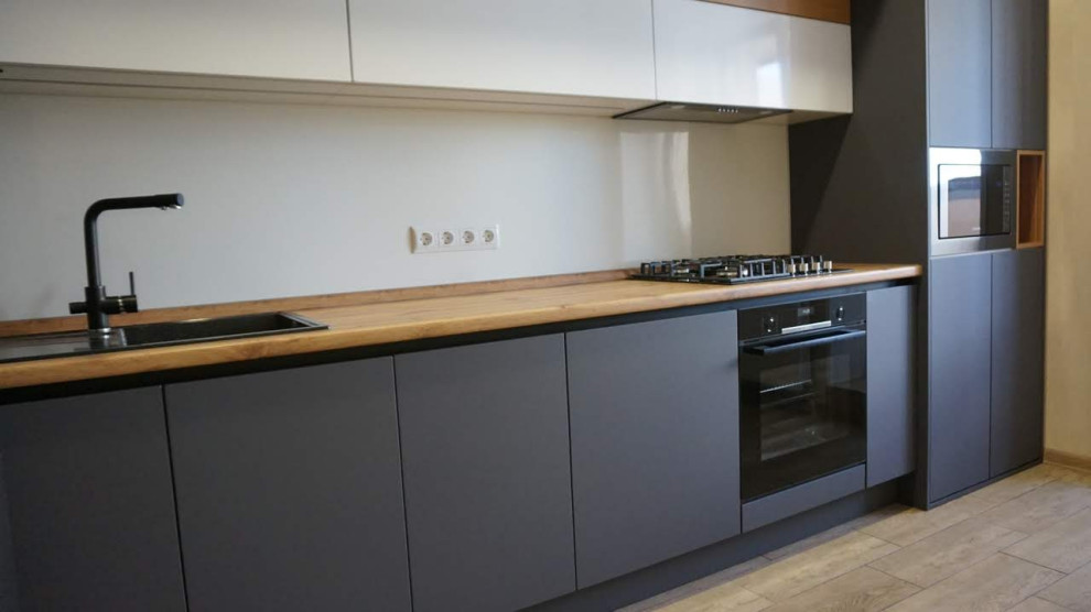 This is an example of a small contemporary single-wall enclosed kitchen in Moscow with a built-in sink, flat-panel cabinets, grey cabinets, wood worktops, white splashback, engineered quartz splashback, black appliances, porcelain flooring, no island, brown floors, brown worktops and all types of ceiling.