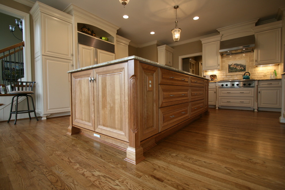 Example of a mid-sized transitional l-shaped light wood floor eat-in kitchen design in Cincinnati with a farmhouse sink, raised-panel cabinets, medium tone wood cabinets, granite countertops, beige backsplash, stone tile backsplash, paneled appliances, brown walls and an island