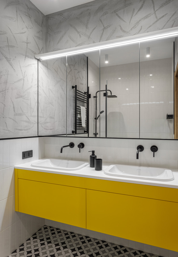 На фото: маленькая главная ванная комната в современном стиле с плоскими фасадами, желтыми фасадами, ванной в нише, инсталляцией, белой плиткой, керамической плиткой, серыми стенами, полом из керамогранита, раковиной с несколькими смесителями, столешницей из искусственного камня, черным полом, белой столешницей, нишей, тумбой под две раковины и встроенной тумбой для на участке и в саду