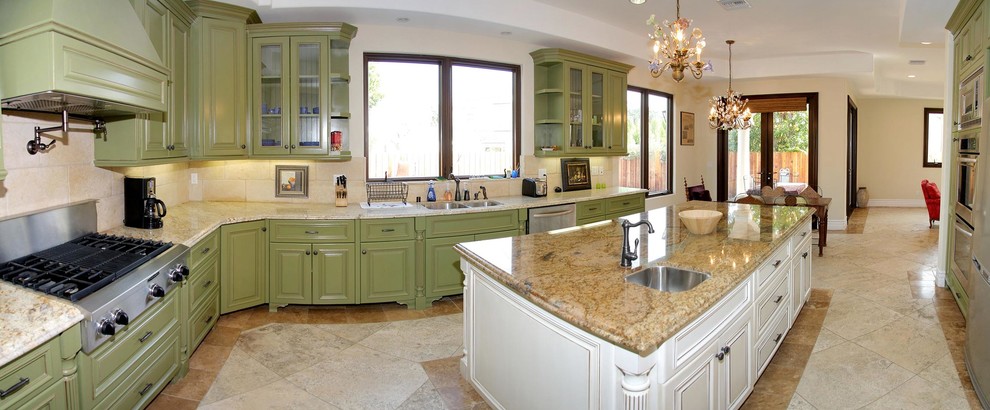 Design ideas for a large mediterranean l-shaped eat-in kitchen in Los Angeles with a drop-in sink, raised-panel cabinets, green cabinets, limestone benchtops, beige splashback, limestone splashback, stainless steel appliances, ceramic floors, with island, beige floor and beige benchtop.