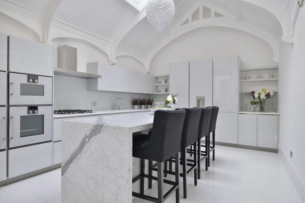 Mid-sized contemporary l-shaped kitchen in Gloucestershire with flat-panel cabinets, white cabinets, white splashback, glass sheet splashback, panelled appliances, with island and white floor.