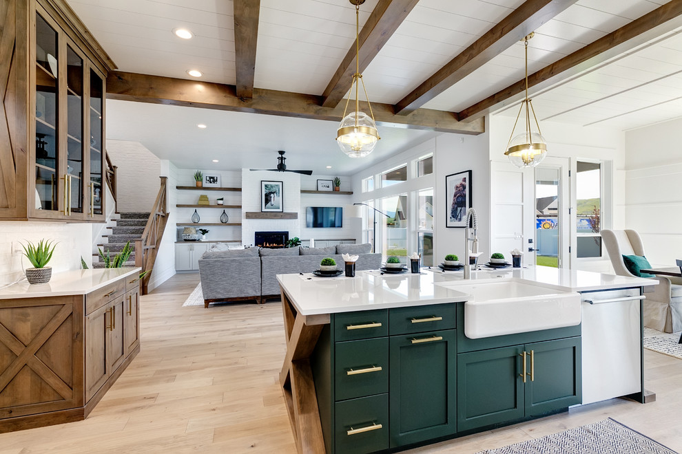 Large country l-shaped open plan kitchen in Boise with a farmhouse sink, shaker cabinets, white cabinets, quartz benchtops, white splashback, subway tile splashback, stainless steel appliances, light hardwood floors, with island, beige floor and white benchtop.