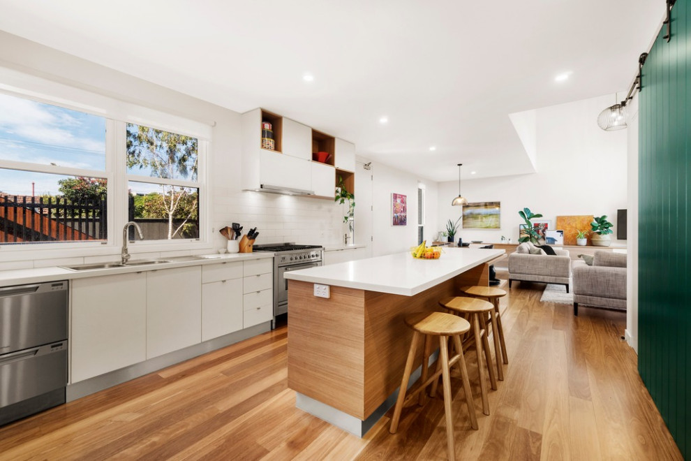 Inspiration for a modern galley kitchen pantry in Melbourne with a double-bowl sink, white cabinets, quartz benchtops, white splashback, ceramic splashback, stainless steel appliances, light hardwood floors, with island and beige benchtop.
